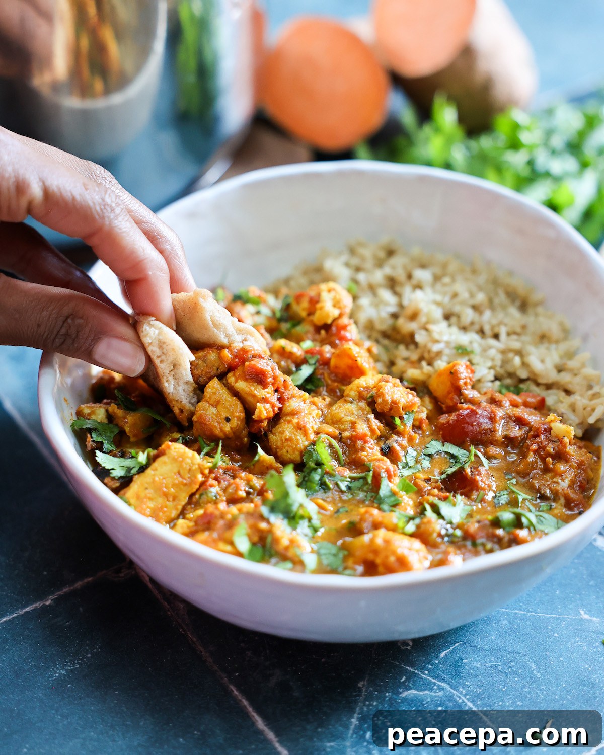 Hand dipping naan into a bowl of vegan tikka masala.