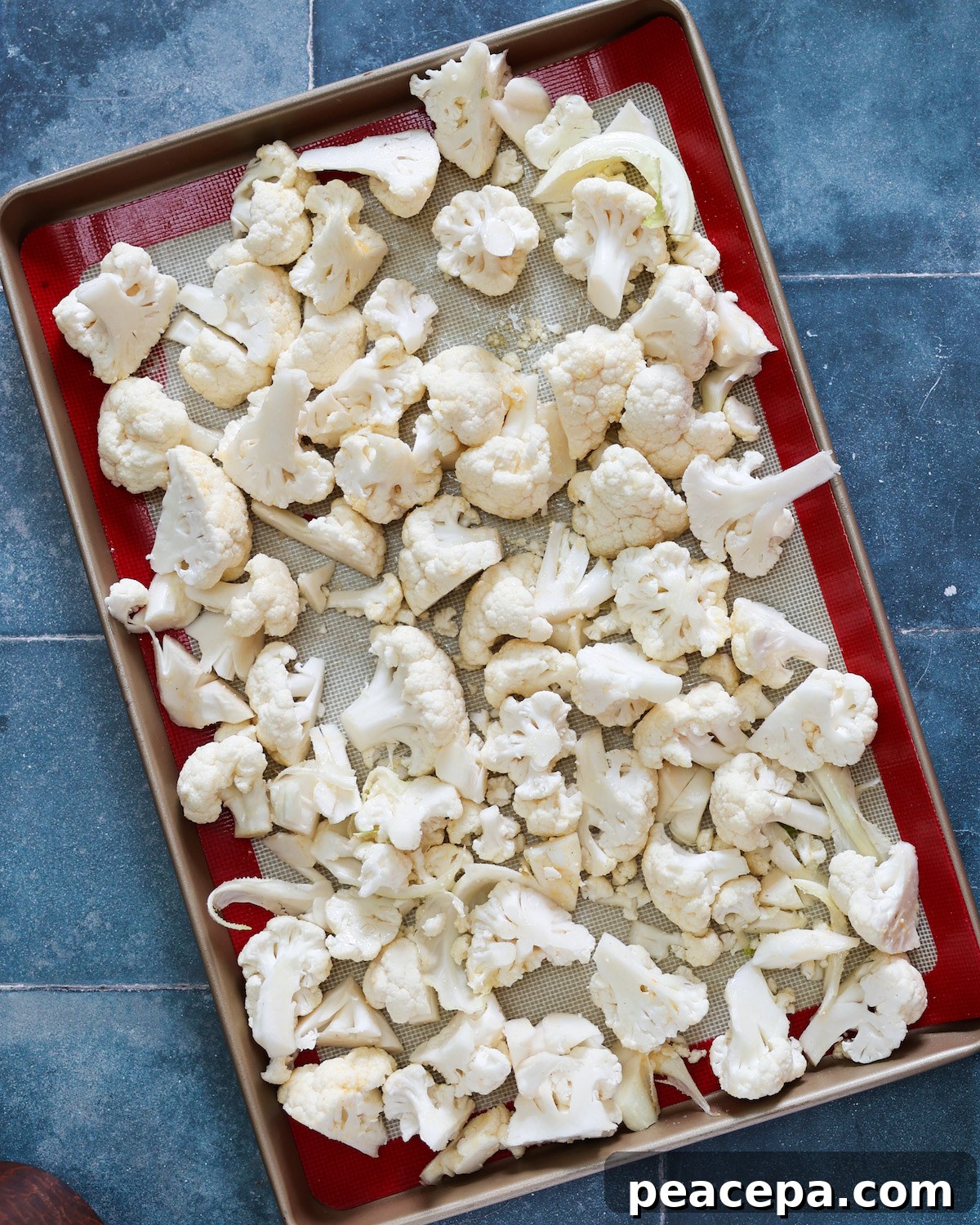 Raw cauliflower on a baking sheet on top of a blue tile counter.