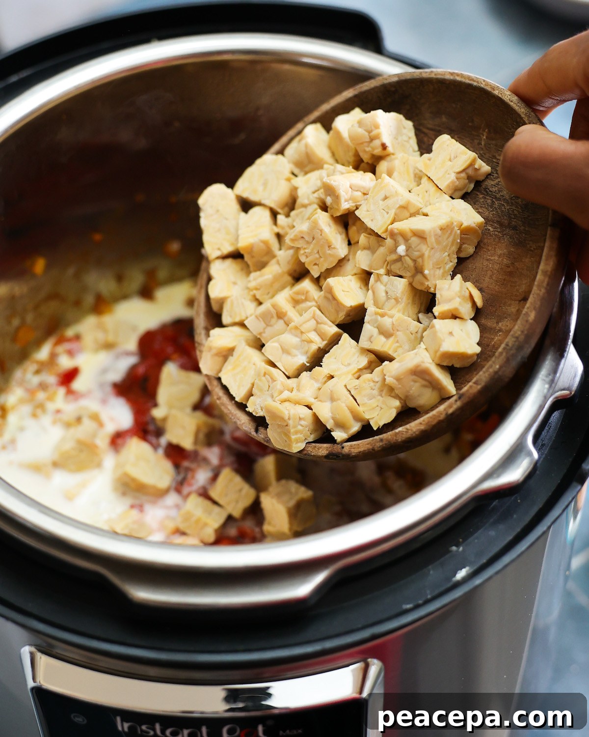 Adding raw tempeh to a pot of vegan tikka masala.