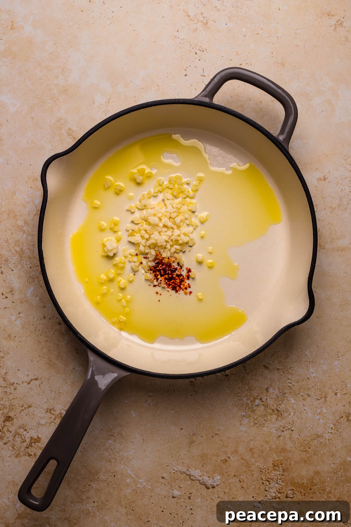 A large skillet with olive oil, garlic, and red pepper flakes.