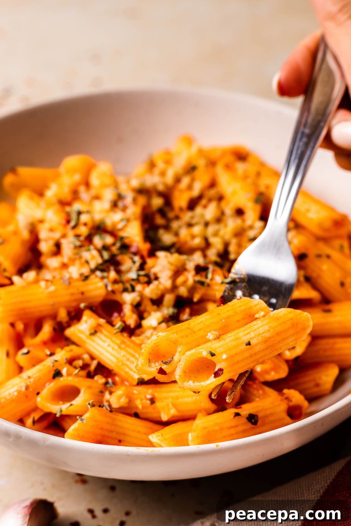 A brown hand taking a bite of the penne arrabbiata.
