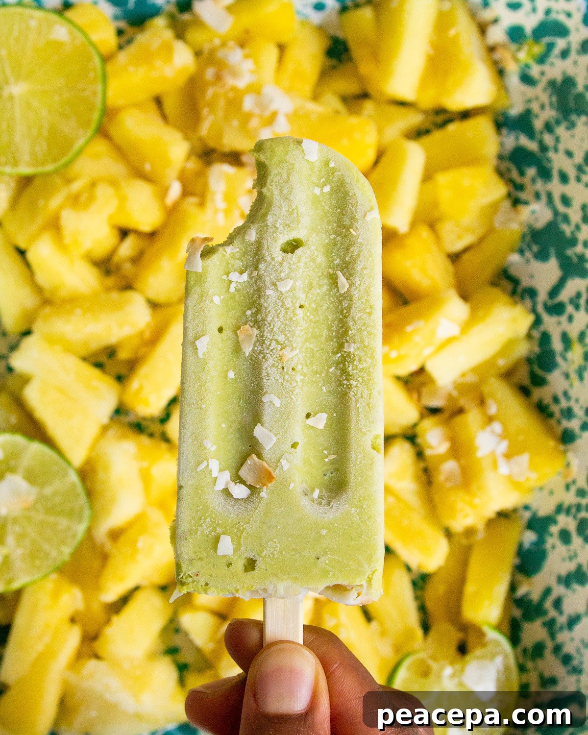 A closeup overhead shot of a brown hand holding an avocado pineapple popsicle with a bite taken out of it.