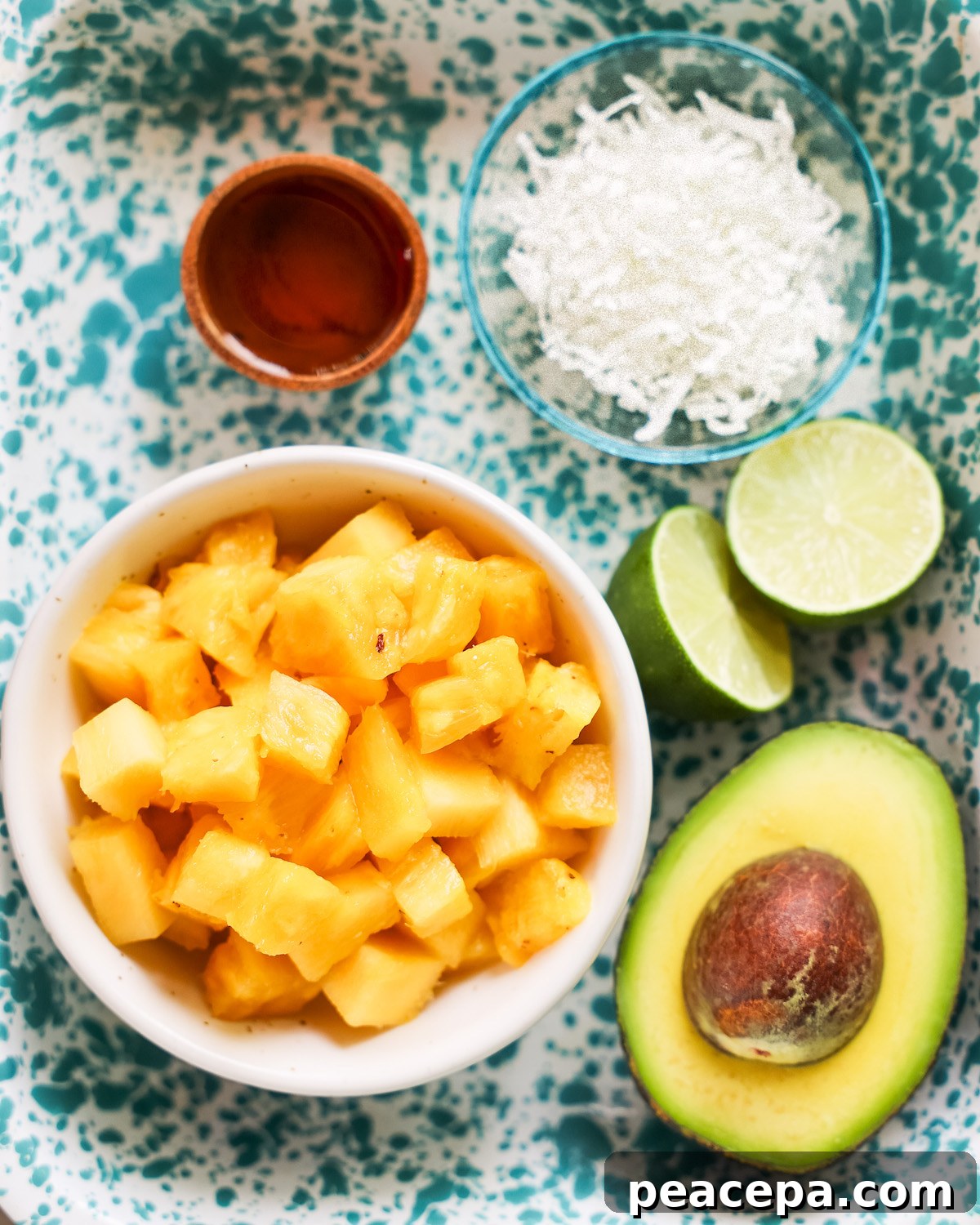 Cubed pineapple, avocado, line, agave syrup, and dried coconut on a speckled blue platter.