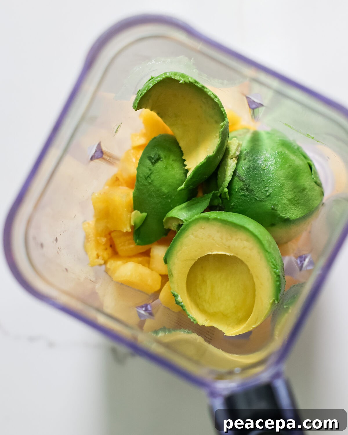 An overhead shot of a blender with avocado and pineapple.