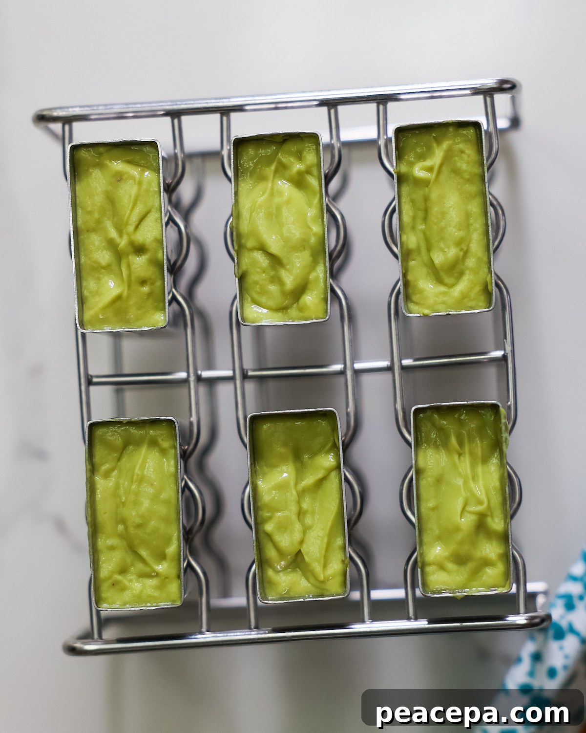 An overhead shot of the avocado pineapple mixture in the popsicle mold.