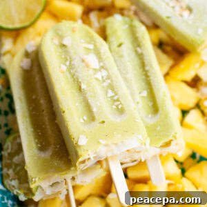 A close-up shot of three avocado pineapple popsicles on a plate of frozen pineapple chunks.