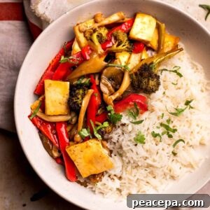 An overhead shot of a white bowl of maple teriyaki tofu and veggies garnished with chopped cilantro.