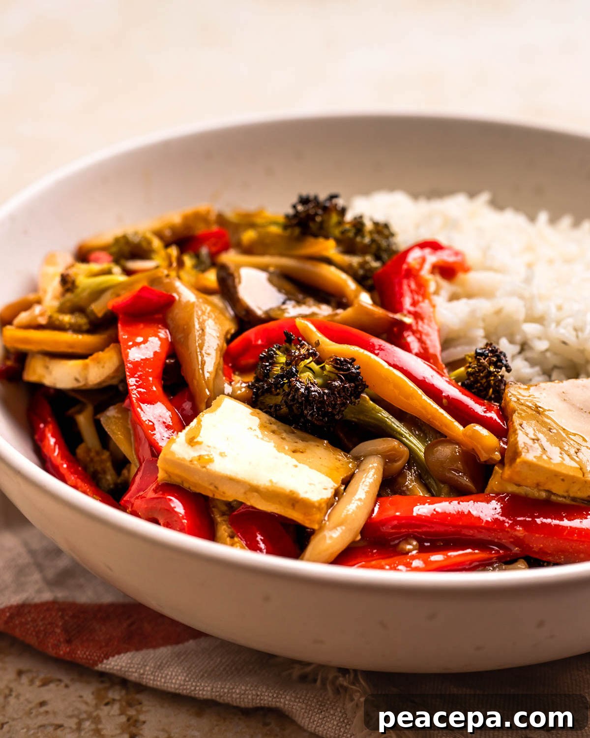 A close-up side shot of a bowl of maple teriyaki tofu and veggies with rice.