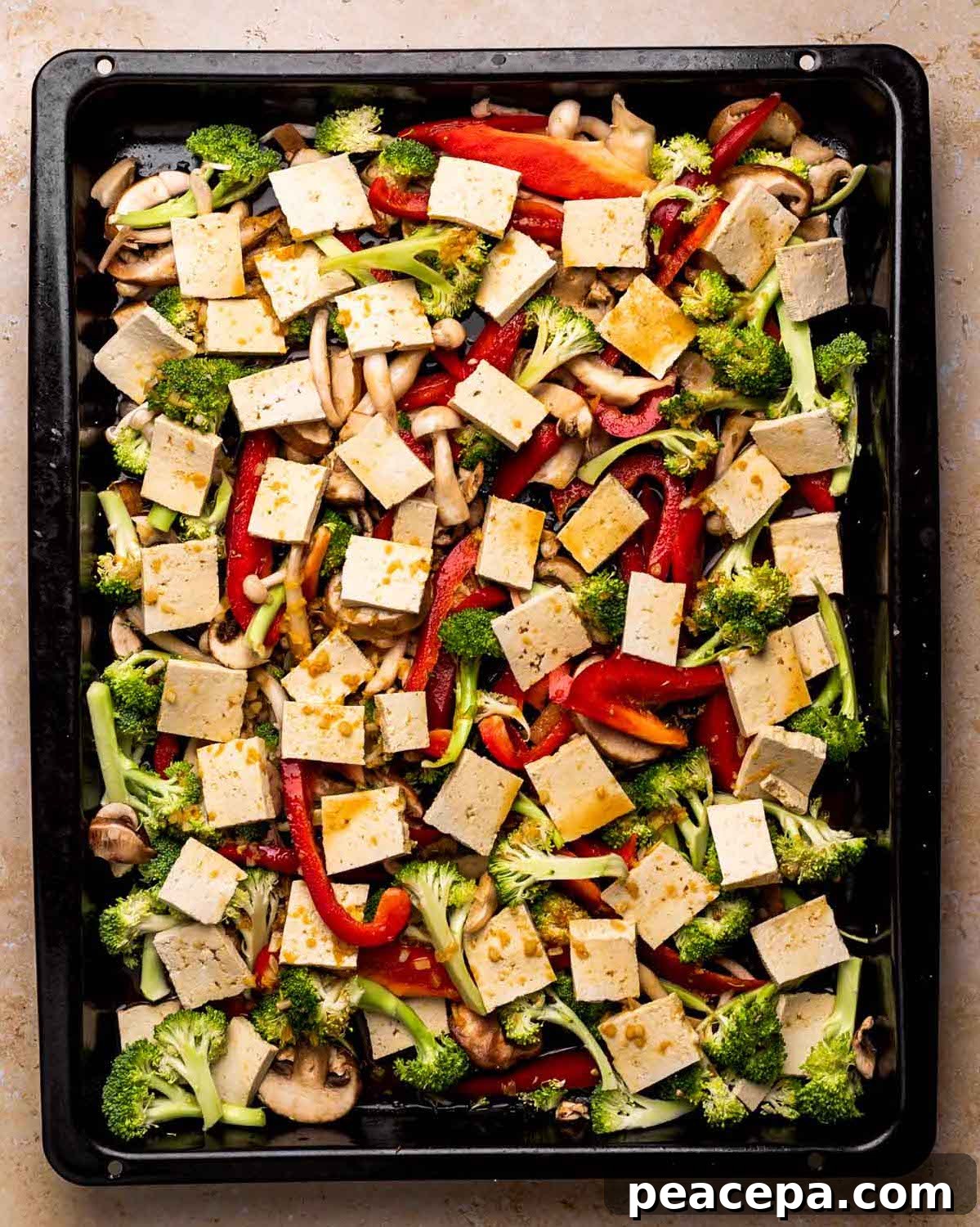 An overhead shot of a baking sheet of veggies with sliced tofu pieces.