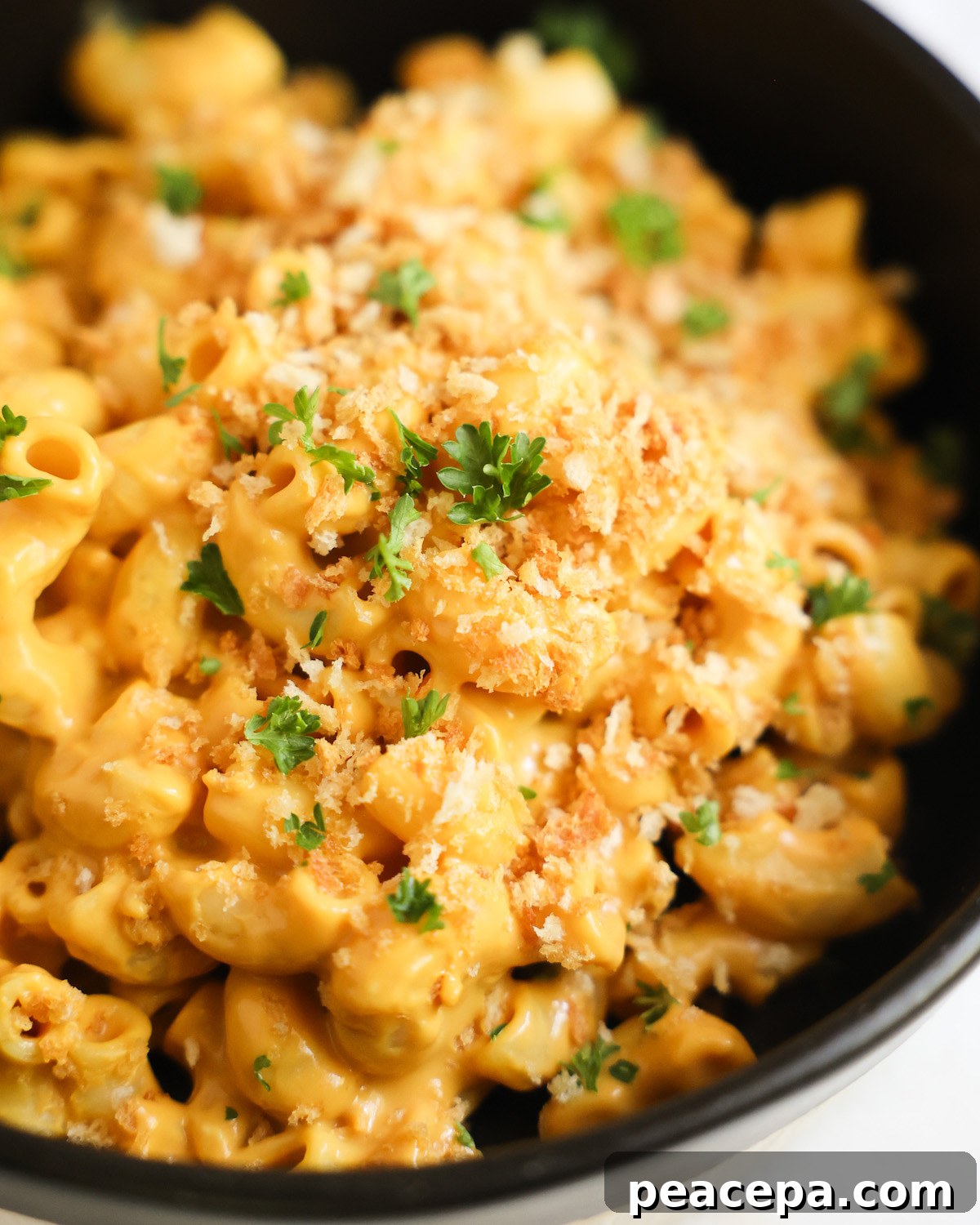 An up-close shot of a black dish of vegan butternut squash mac and cheese with breadcrumbs and minced parsley.