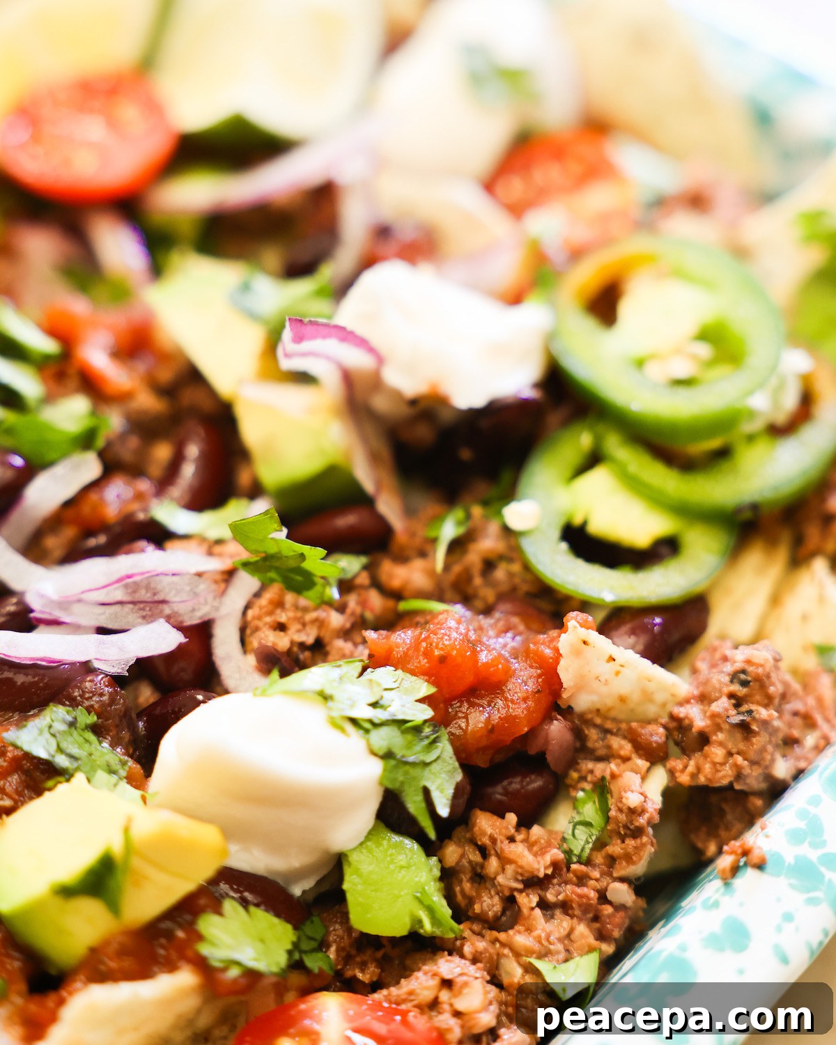 A close up shot of vegan nachos with vegan sour cream, avocados, and jalapeños.