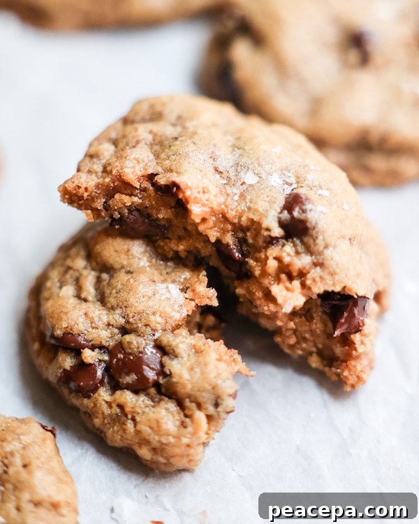 An up-close shot of a vegan chocolate chip cookie broken into two on a white counter.