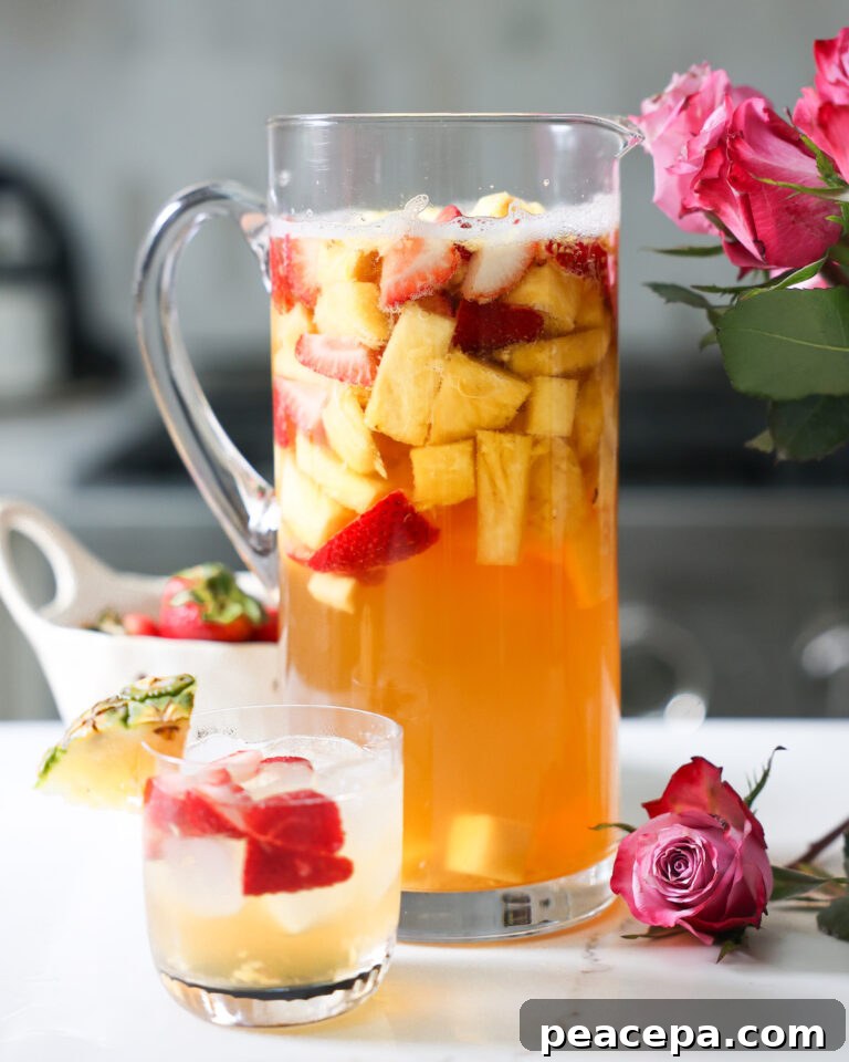 A pitcher and small glass of pineapple summer sangria on the counter with roses.