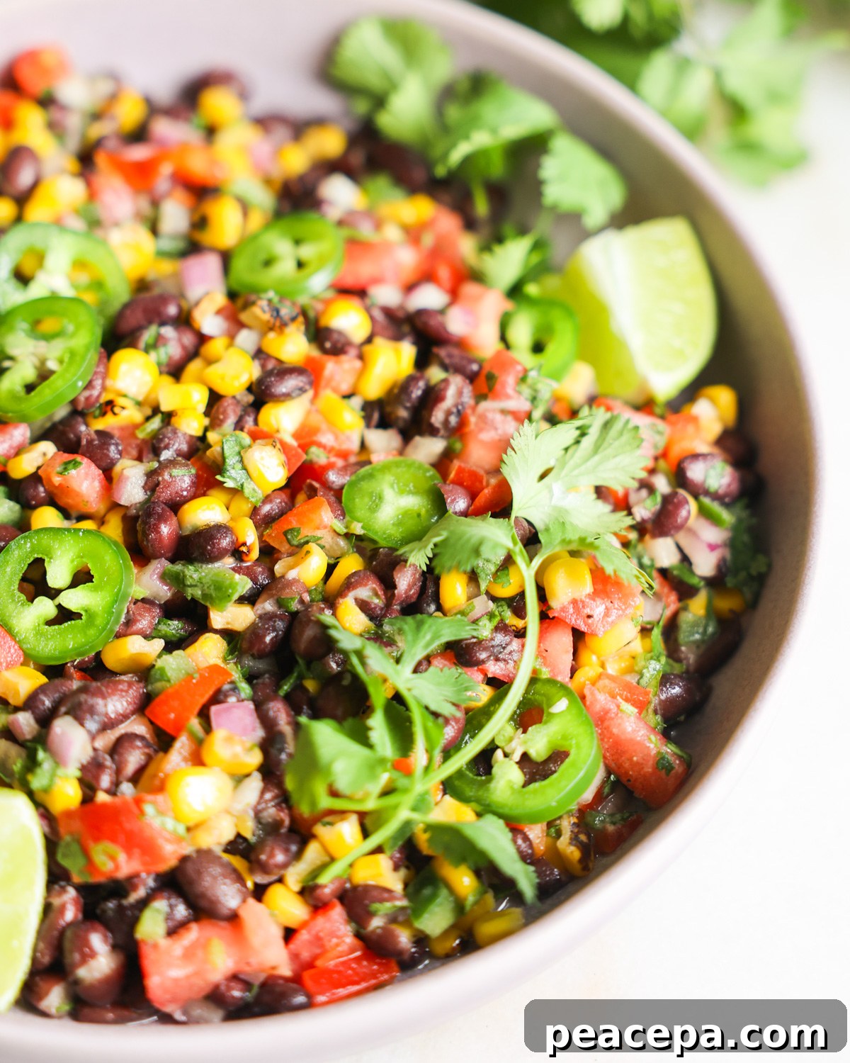 A close-up show of a bowl of black bean and corn salad with jalapenos, cilantro, and lime.