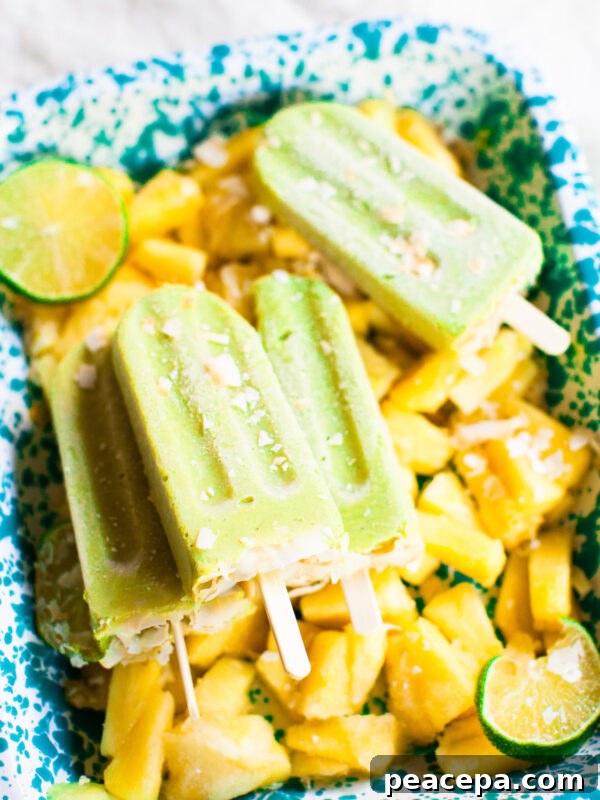 Creamy Homemade Guacamole Recipe for Parties and Dips 13 An angled side shot of avocado pineapple popsicles stacked on a blue tray of frozen pineapple.
